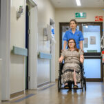 A nurse pushes a patient in a wheelchair down the hospital corridor