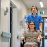 A nurse pushes a patient in a wheelchair down the hospital corridor